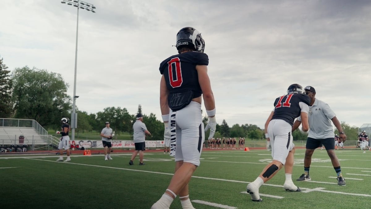 Football players in navy and white uniforms practicing on field during daytime with stadium lights visible