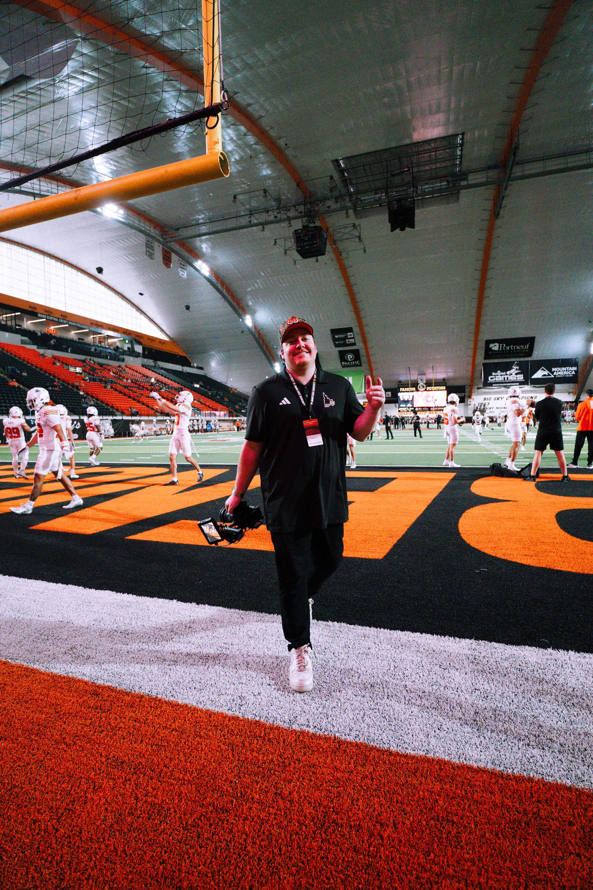 Person in black Adidas gear running on red turf in an indoor sports facility